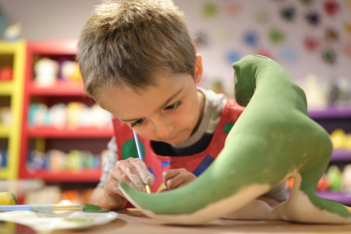 Niño esculpe un dinosaurio con pasta de moldear de plastilina