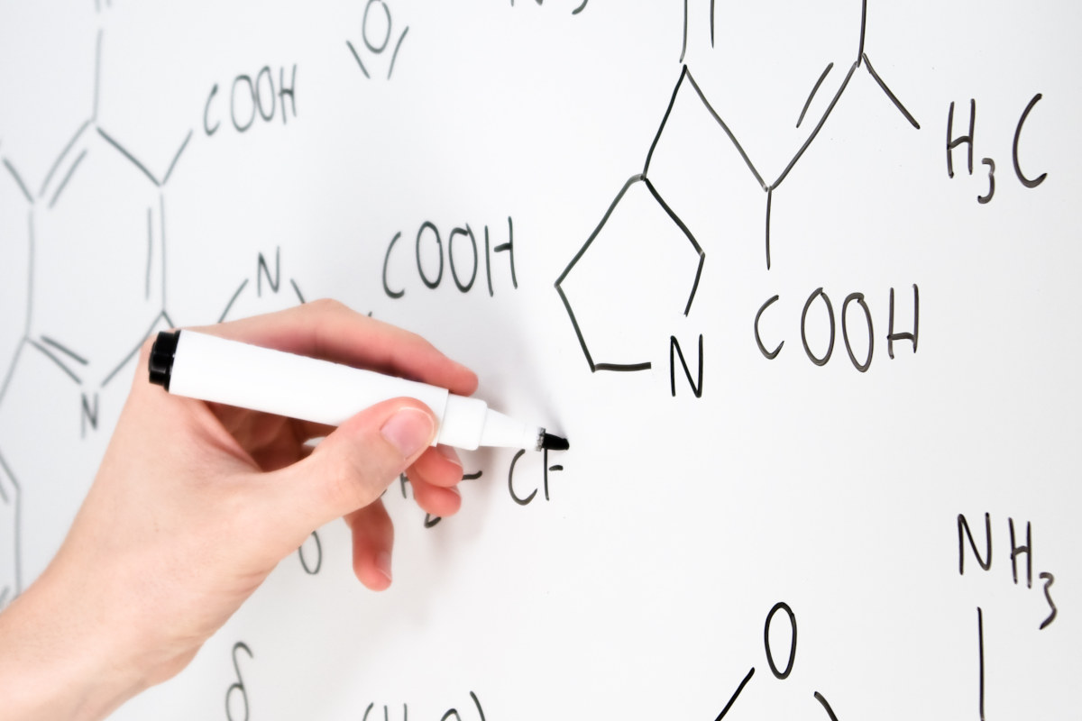 Profesor explica fórmula química con rotulador en una pizarra blanca